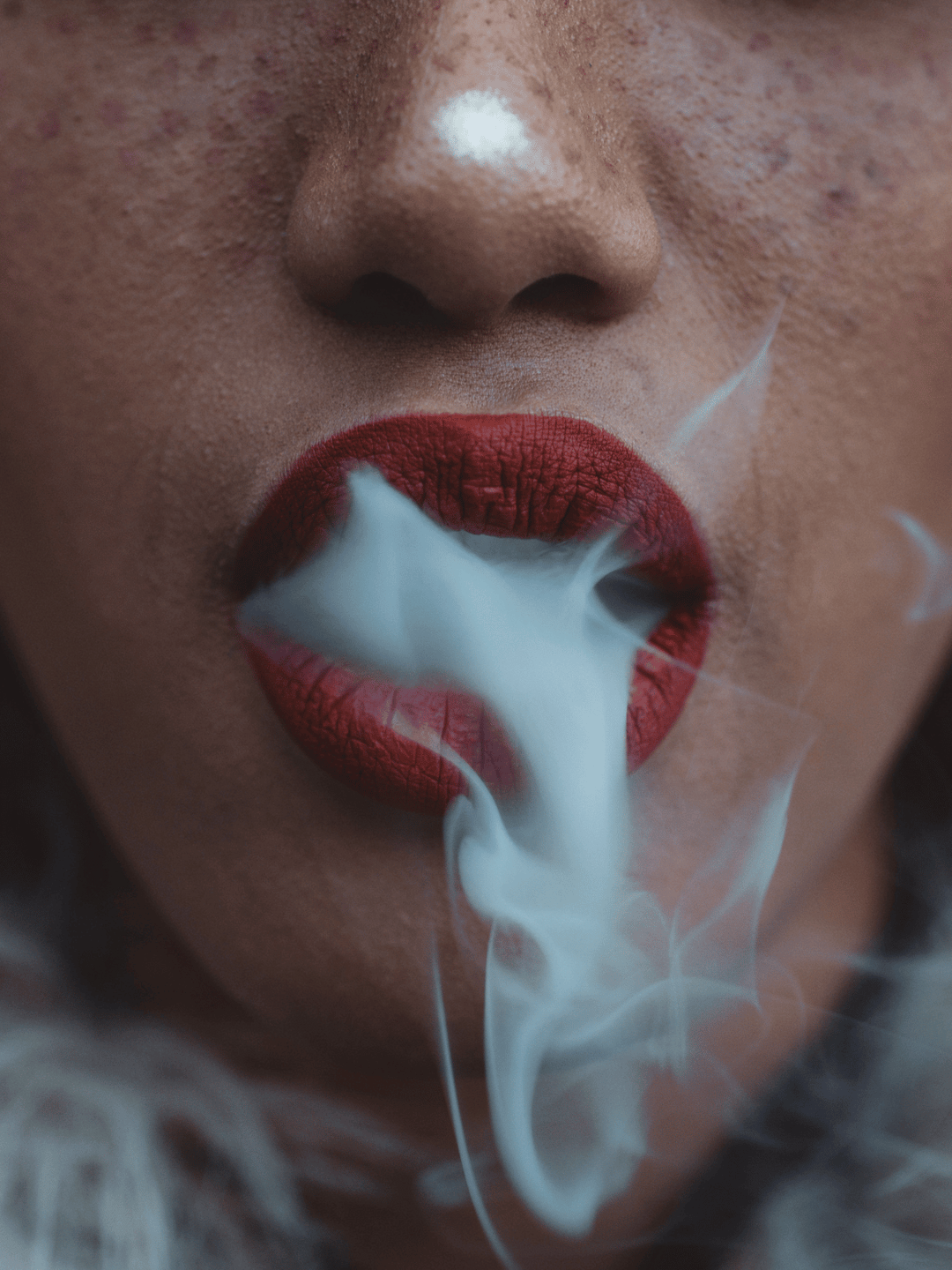 Frau mit rotem Lippenstift die Rauch ausatmet